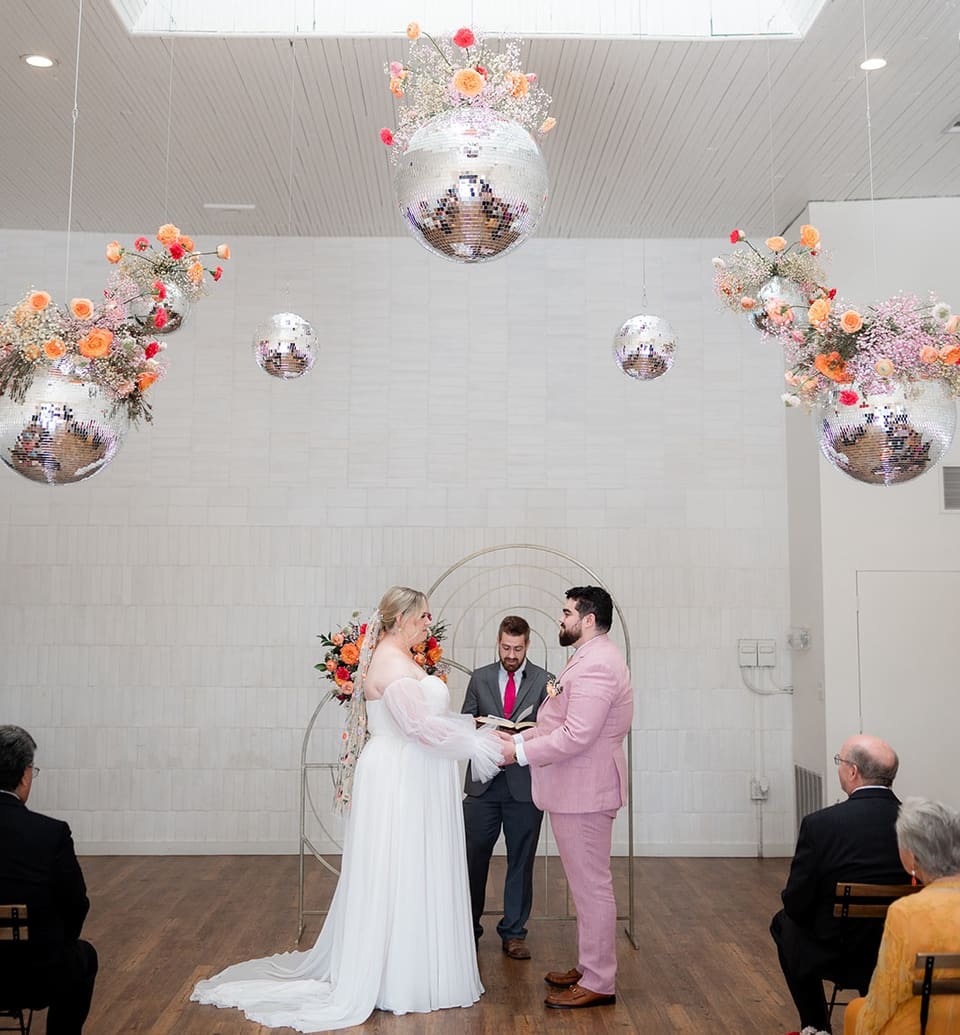 Couple exchanging vows beneath a hanging disco ball floral installation